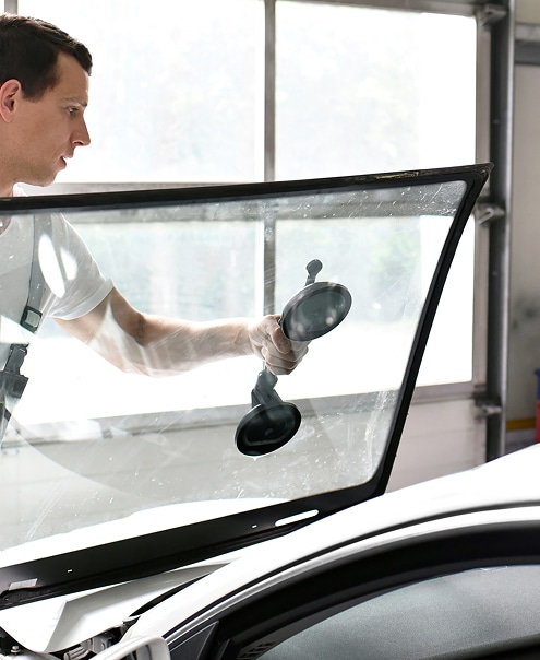 Installation de Pare-brise Auto avec Ventouse : Pose Rapide Technicien en train d'installer un pare-brise de voiture à l'aide d'une ventouse double, mouvement de pose précis dans un atelier.