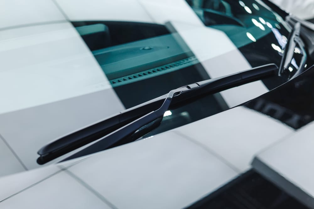 Essuie-glace moderne sur pare-brise de voiture. Essuie-glace noir aérodynamique au repos sur le pare-brise d'une voiture sportive, avec des reflets géométriques brillants sur le capot.