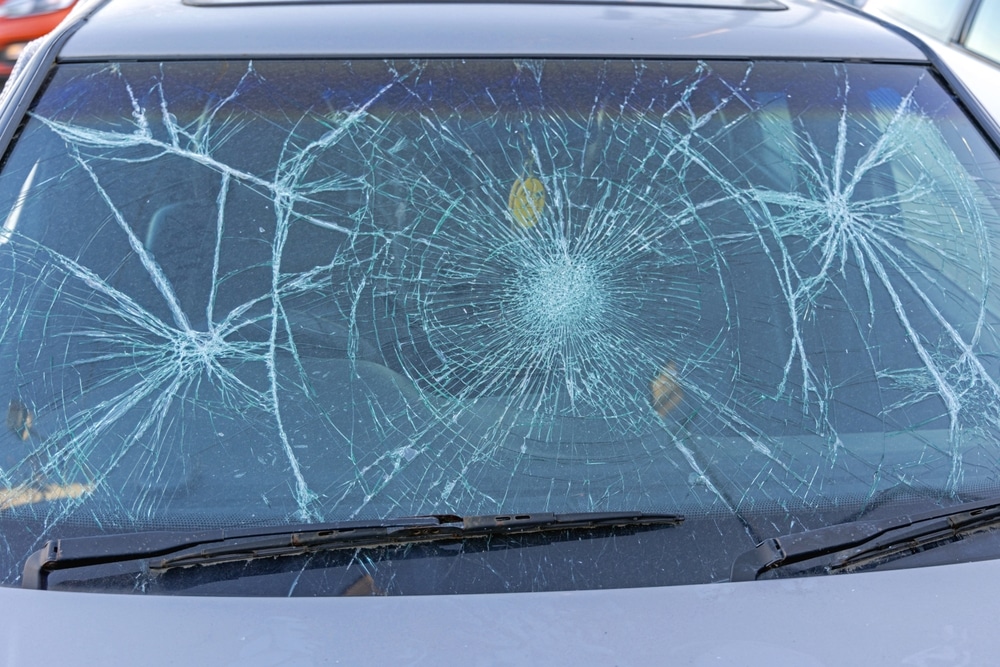 Pare-brise de voiture brisé: impacts et fissures extrêmes. Pare-brise de voiture sévèrement endommagé. Le verre de sécurité est brisé et fissuré en toile d'araignée après plusieurs impacts violents.